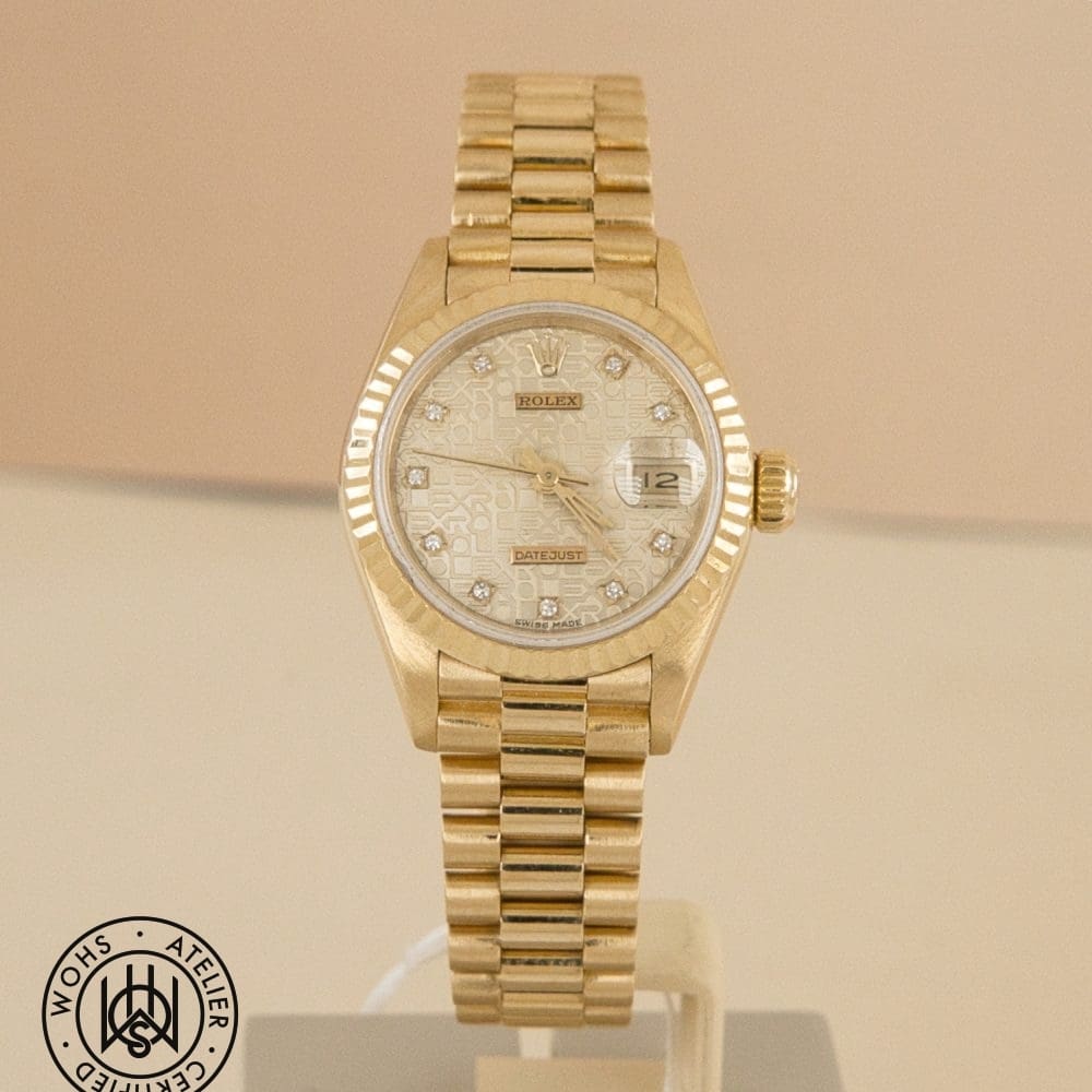 Gold Rolex Datejust wristwatch with diamond hour markers and fluted bezel, shown on a stand with watermark in the corner