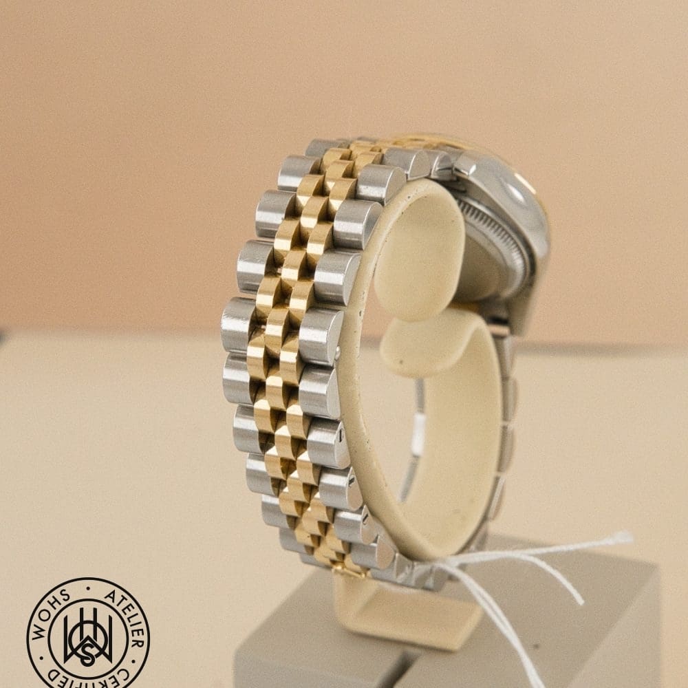 Two-tone gold and stainless steel watch bracelet on a display stand, with a circular brand logo in the bottom left corner. DSC02965