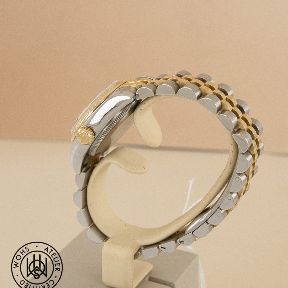 Two-tone gold and silver wristwatch on a beige display stand, shown from the side with crown visible; logo in bottom-left corner. DSC02966