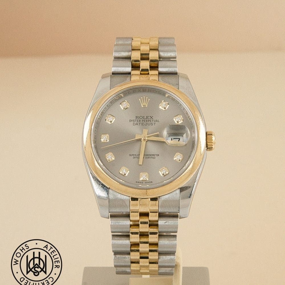 Two-tone Rolex Datejust wristwatch on a stand with diamond hour markers, gold bezel, and two-tone bracelet; date window at 3 o'clock.