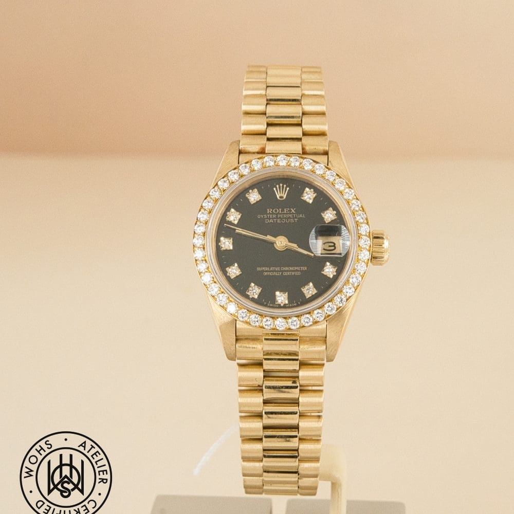Gold Rolex Datejust wristwatch with a diamond-encrusted bezel and black dial on a display stand.