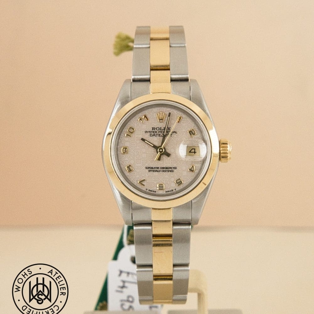 Two-tone Rolex Oyster wristwatch (silver and gold) with date window, facing forward against a beige background.