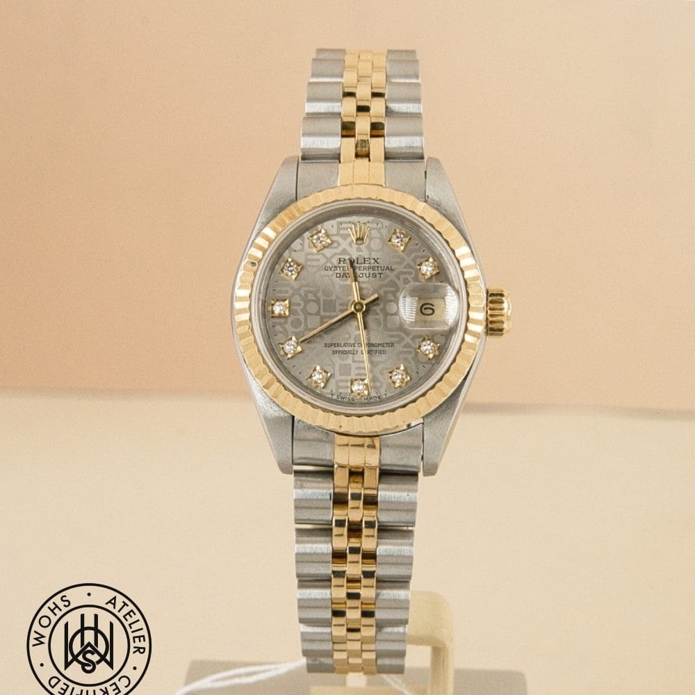 Two-tone Rolex Datejust watch with diamond hour markers and a gold fluted bezel on a beige background.