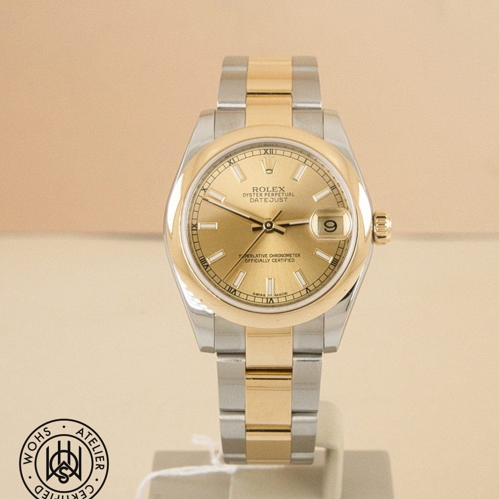 Two-tone Rolex Oyster Perpetual Datejust wristwatch with gold dial on a display stand, showing date window at 3 o'clock.