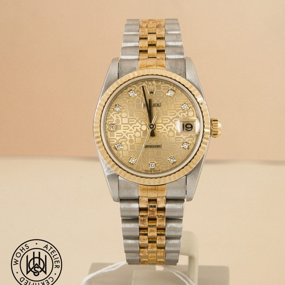 Two-tone Rolex Datejust watch with a gold fluted bezel, diamond hour markers, and a two-tone bracelet on a beige background, close-up display
