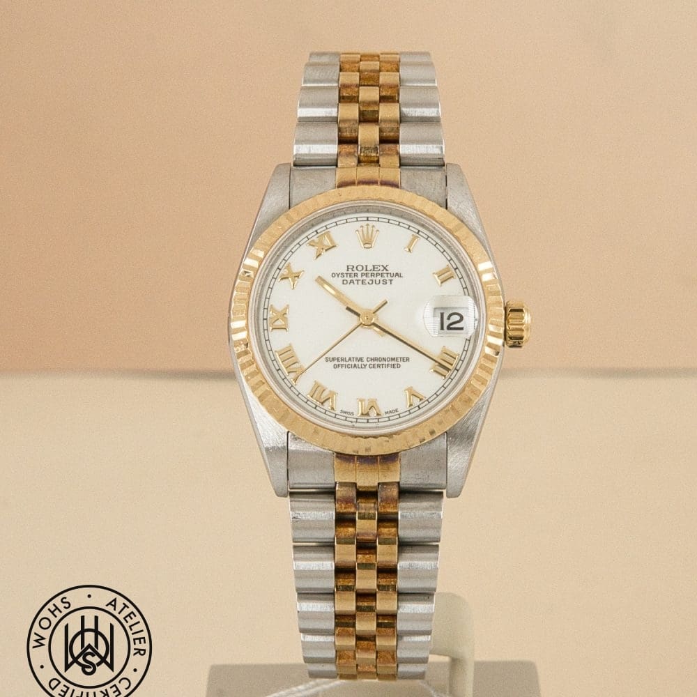 Two-tone Rolex Datejust wristwatch with white dial, gold Roman numerals, and gold bezel, showing date at 3 o'clock.