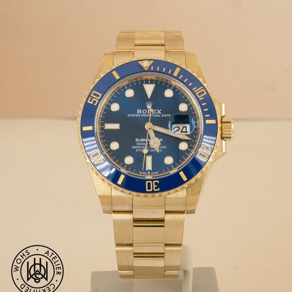 Gold Rolex Submariner wristwatch with blue bezel on display, date visible at 3 o'clock.