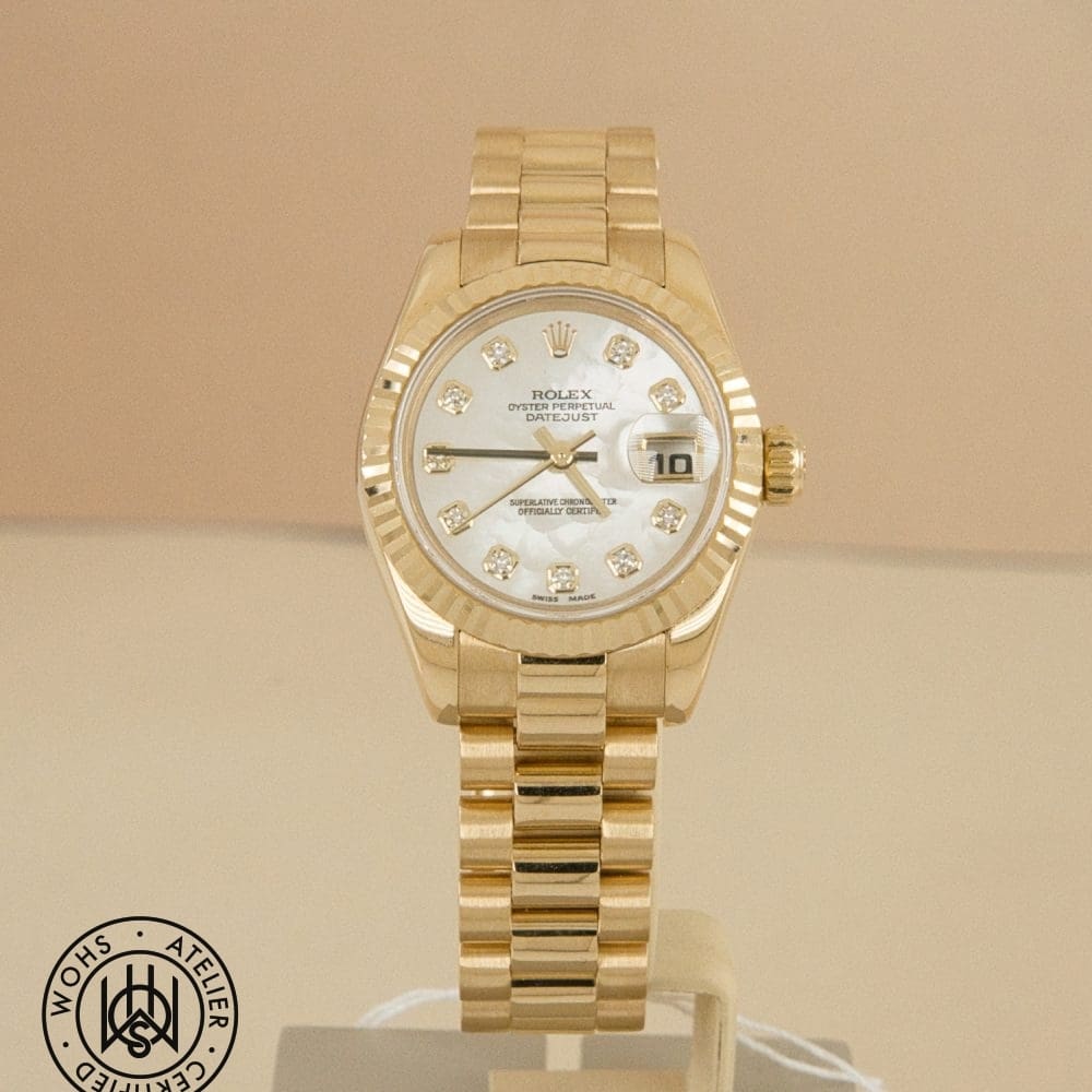 Gold Rolex Oyster Perpetual Datejust wristwatch with diamond hour markers on a white dial and date window at 3 o'clock, shown on a display stand.