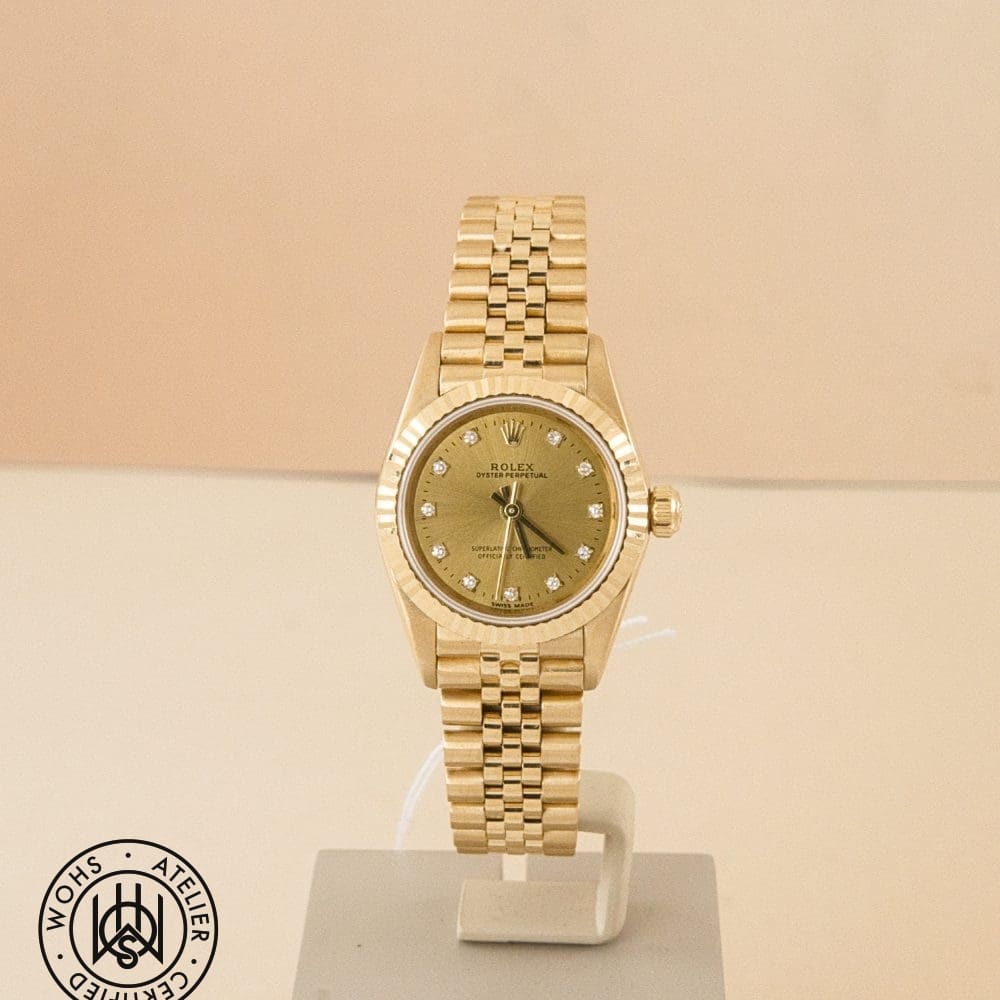 Gold Rolex Oyster Perpetual wristwatch on a display stand with diamond hour markers and fluted bezel.