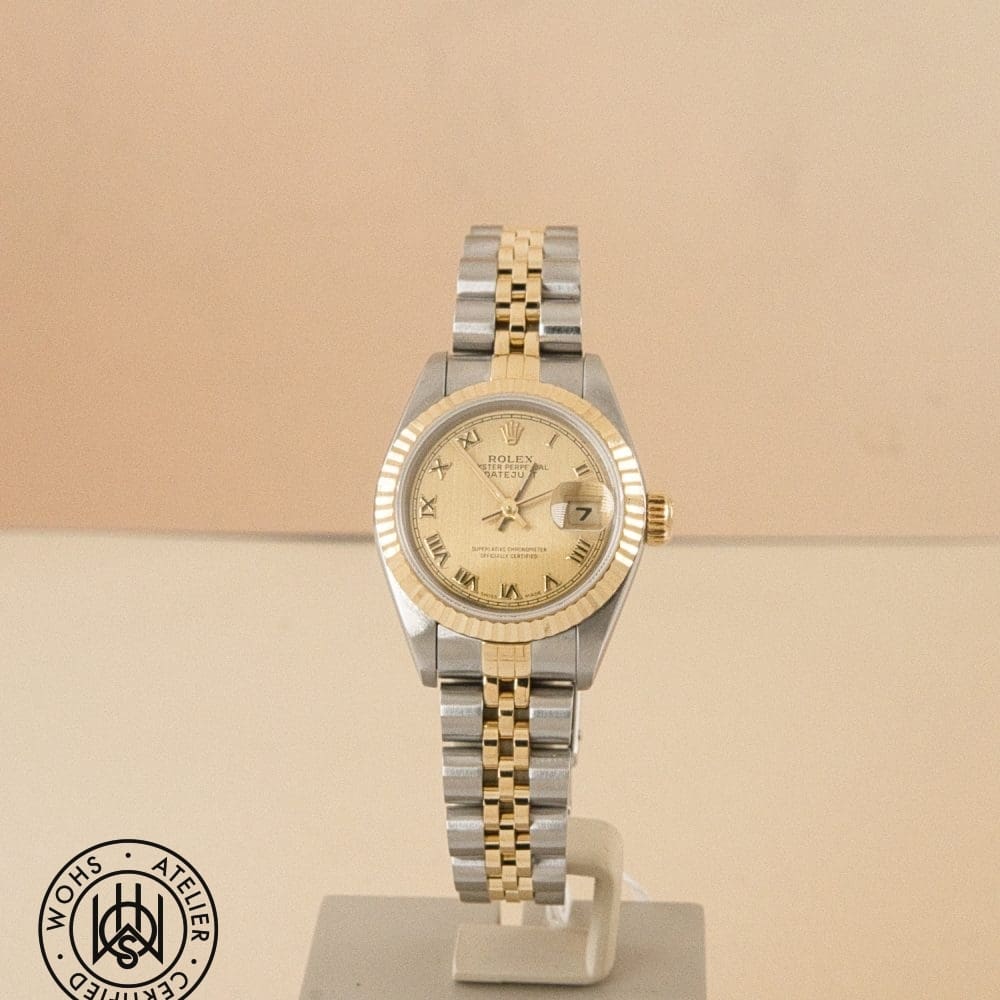 Two-tone Rolex Datejust wristwatch on a display stand, gold and silver bracelet, gold dial with Roman numerals and date window at 3 o'clock.