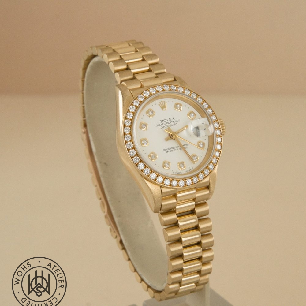 Gold Rolex wristwatch with diamond-encrusted bezel and white dial on display, date window at 3 o'clock, luxury timepiece centerpiece. DSC03309