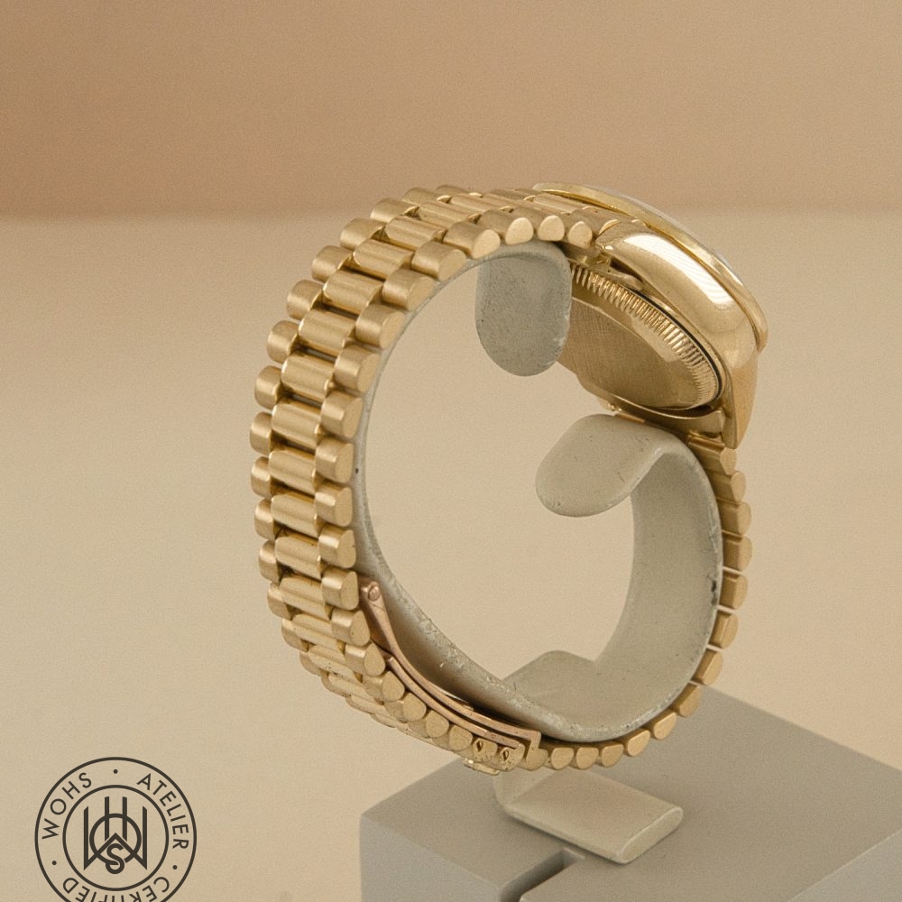Gold-tone metal watch bracelet with rounded links displayed on a stand, logo visible in lower-left corner DSC03310