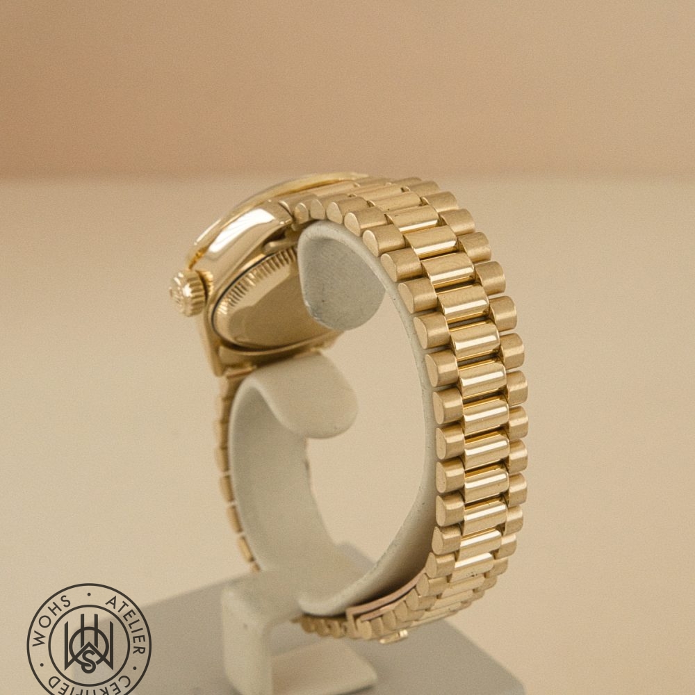Gold-toned metal link wristwatch on a display stand, side view with crown visible; watermark in bottom-left corner. DSC03311