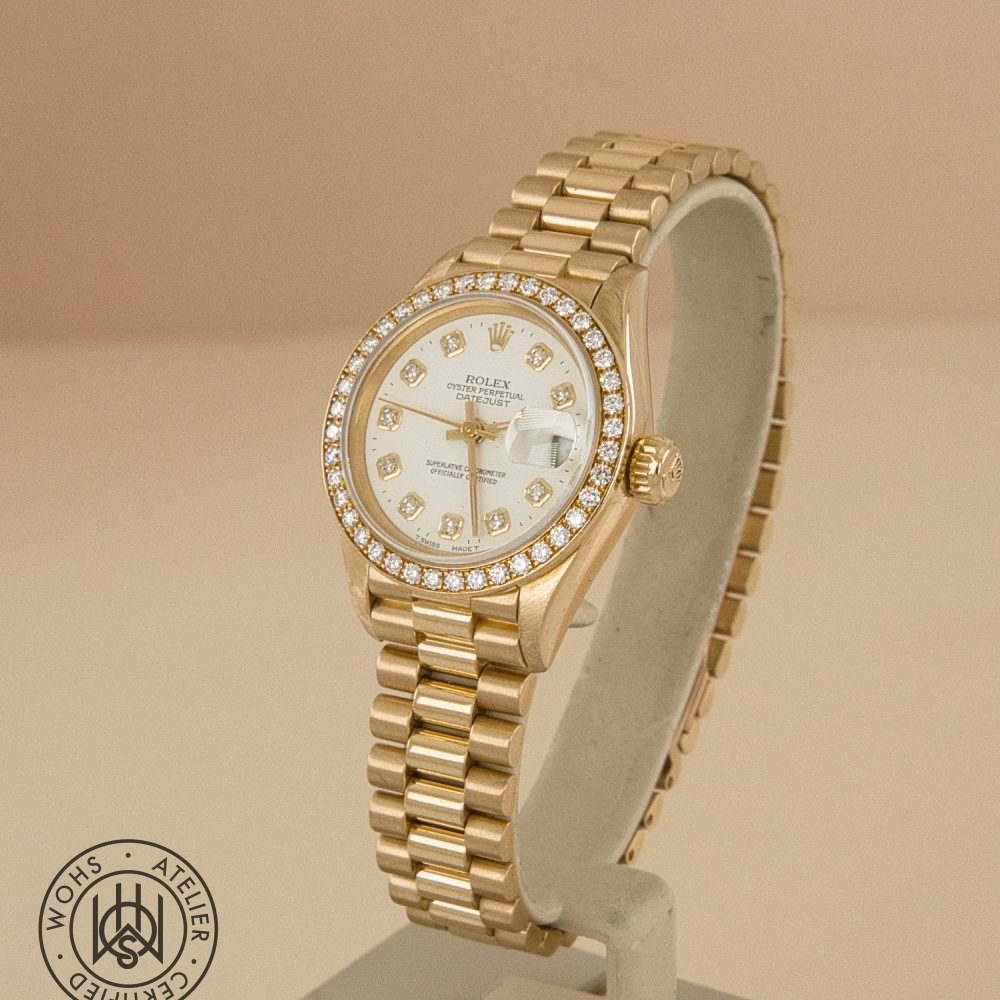 Gold Rolex Datejust wristwatch with a diamond-studded bezel and diamond hour markers on a gold bracelet, displayed upright on a stand. DSC03312