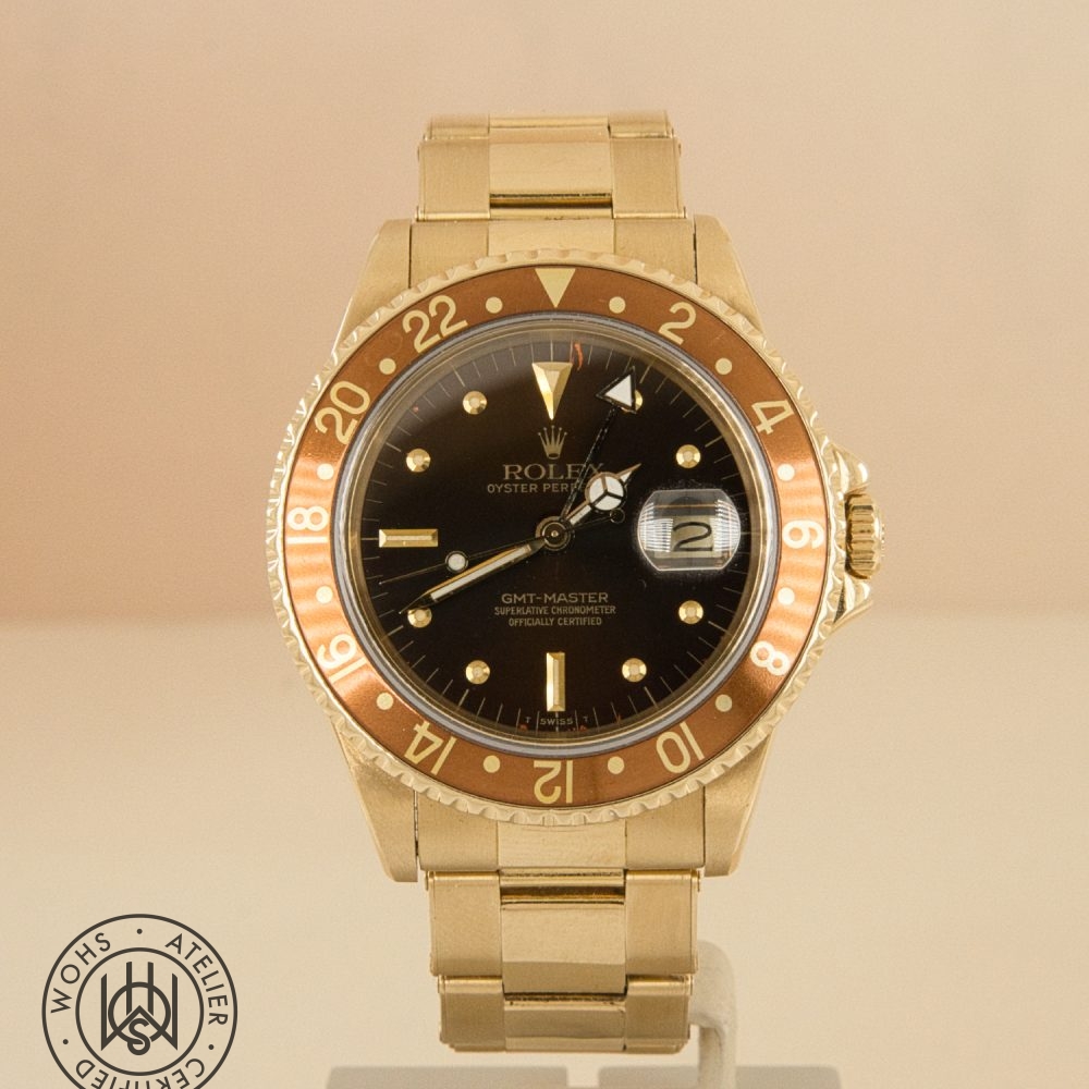 Gold Rolex GMT-Master wristwatch with black dial and brown 24-hour bezel, date window magnified on the right, gold bracelet visible at 6 o'clock position. DSC03313
