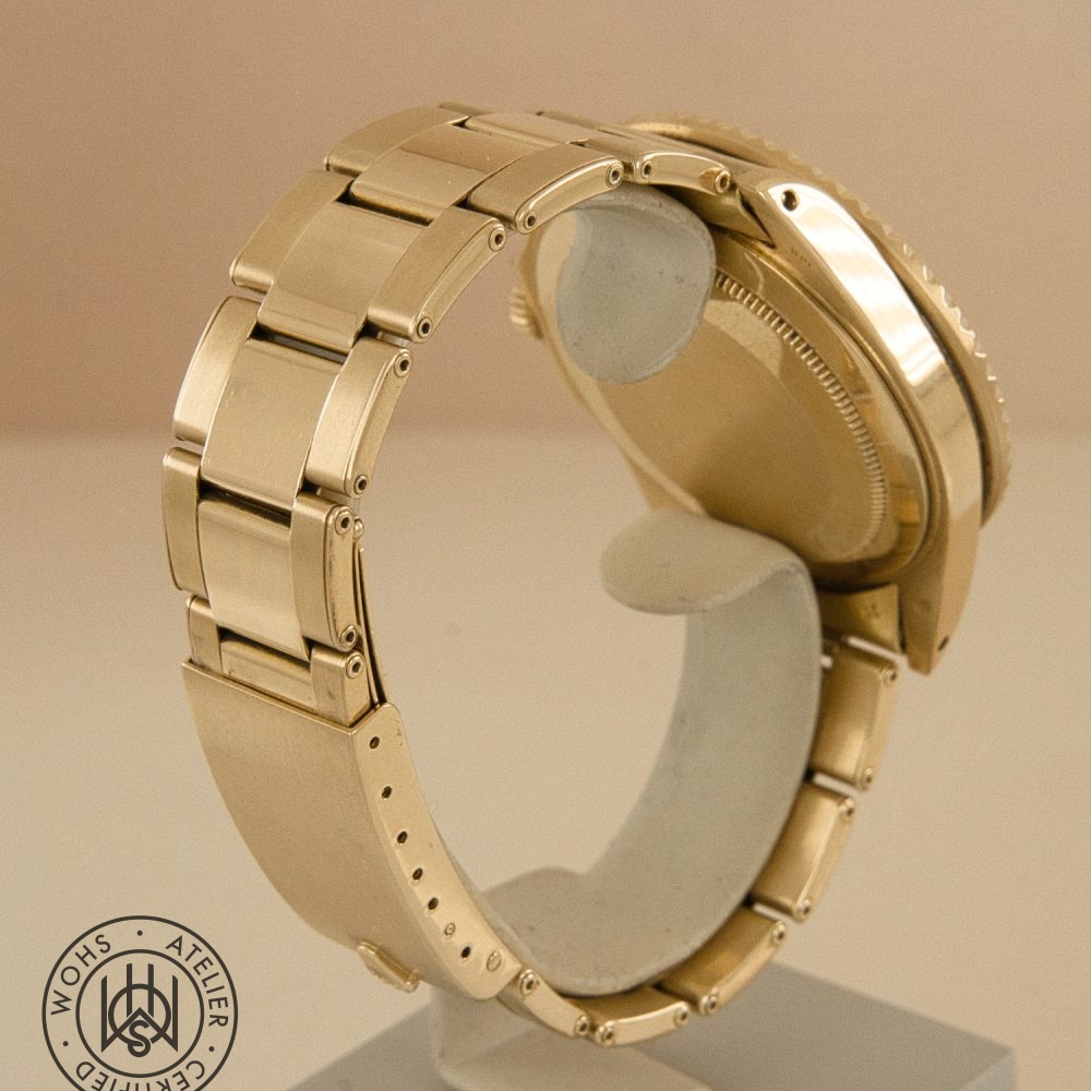 Close-up of a gold metal watch bracelet and clasp, viewed from the side on a stand, with a circular WOHS Atelier logo in the lower left corner. DSC03315