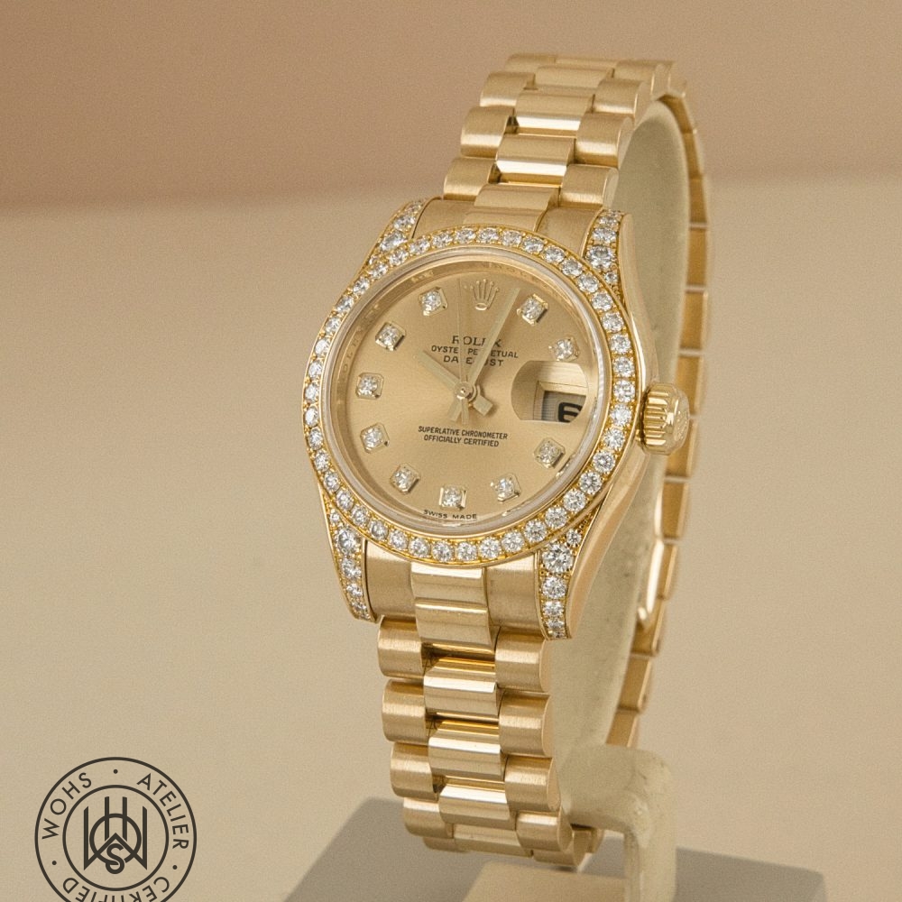 Gold Rolex watch with diamond-encrusted bezel displayed on a stand, face showing date window and diamond hour markers. Preowned Rolex Lady Datejust reference 179158 factory set lugs and bezel 1