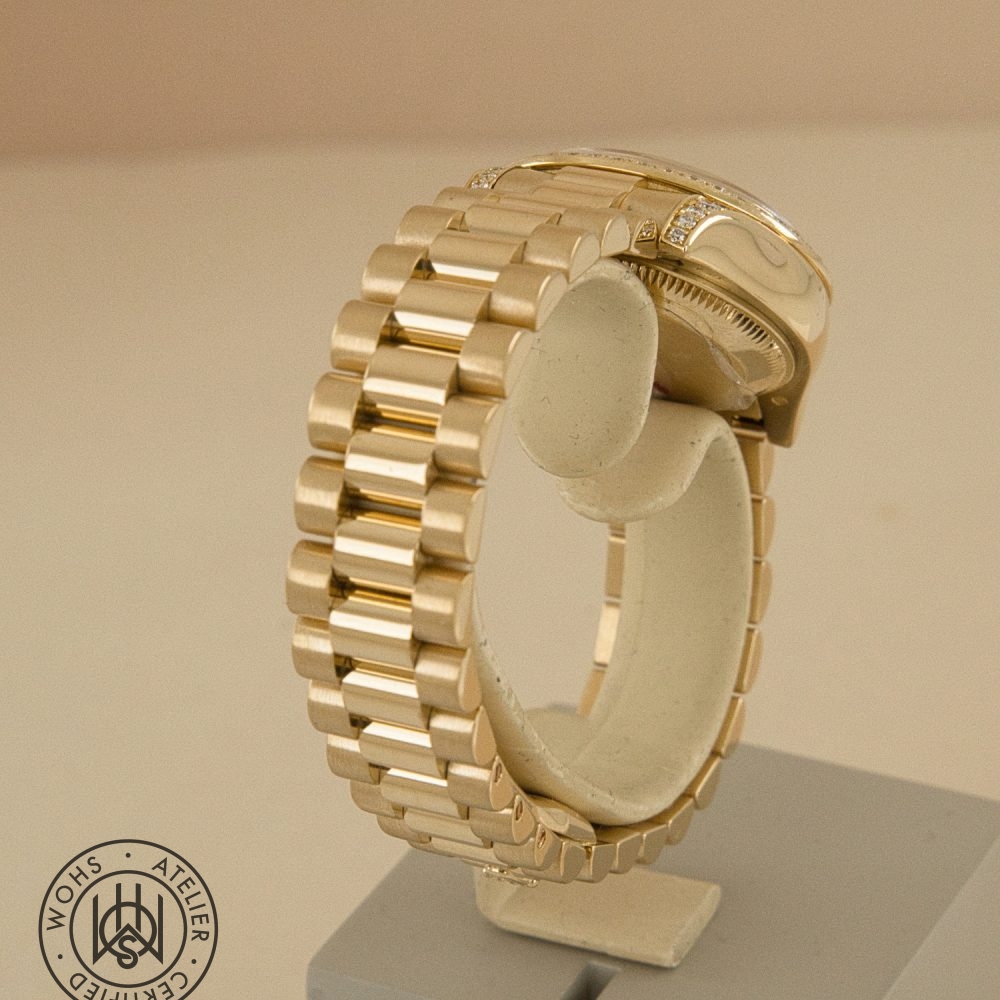 Gold wristwatch with a tall, multi-link gold bracelet displayed on a white stand; a circular stamp sits at the bottom left of the image indicating certification. Preowned Rolex Lady Datejust reference 179158 factory set lugs and bezel 5