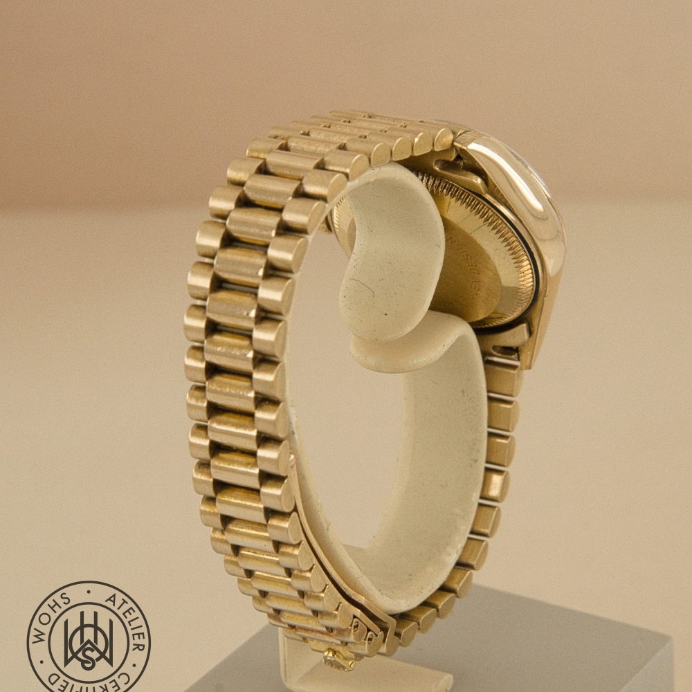 Close-up of a gold wristwatch bracelet on a display stand, showing polished links and clasp area with a circular workshop seal in the corner Rolex Ladies Datejust 26mm 69178 Diamond Hour and Pave set markers 18ct dial 4