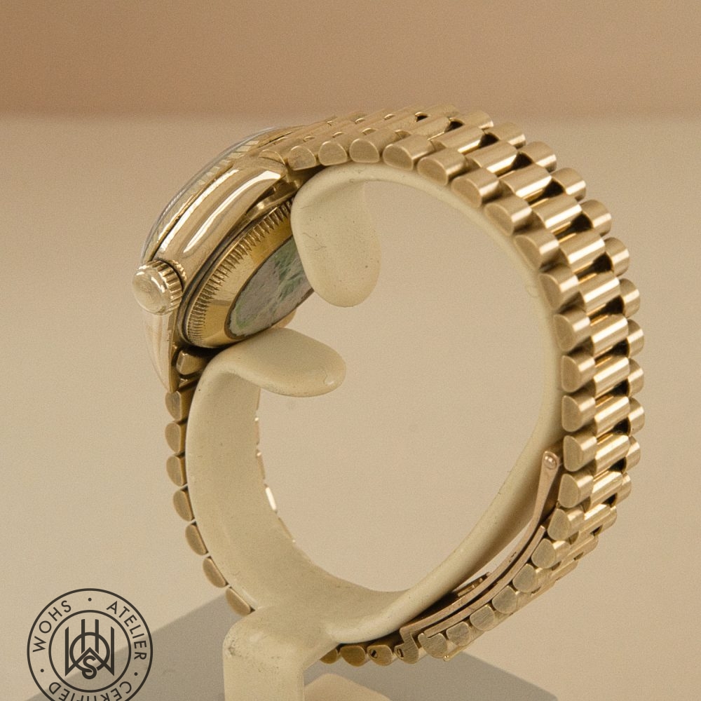 Close-up of a gold wristwatch on a display stand, showing the side crown and segmented bracelet; certification stamp in the bottom left corner. Rolex Ladies Datejust reference 69178 - Diamond and Ruby Dial Pave 18ct Gold Dial 5