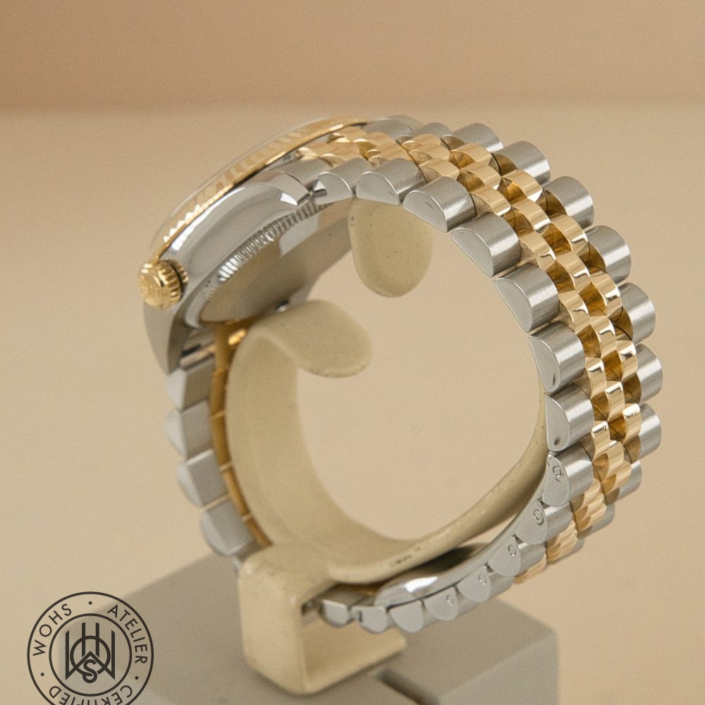 Close-up side view of a two-tone gold and silver metal watch bracelet on a display stand, with a circular WoHS/attestation stamp visible in the bottom left corner. Used Ladies Rolex datejust reference 178273 champange diamond dial 6